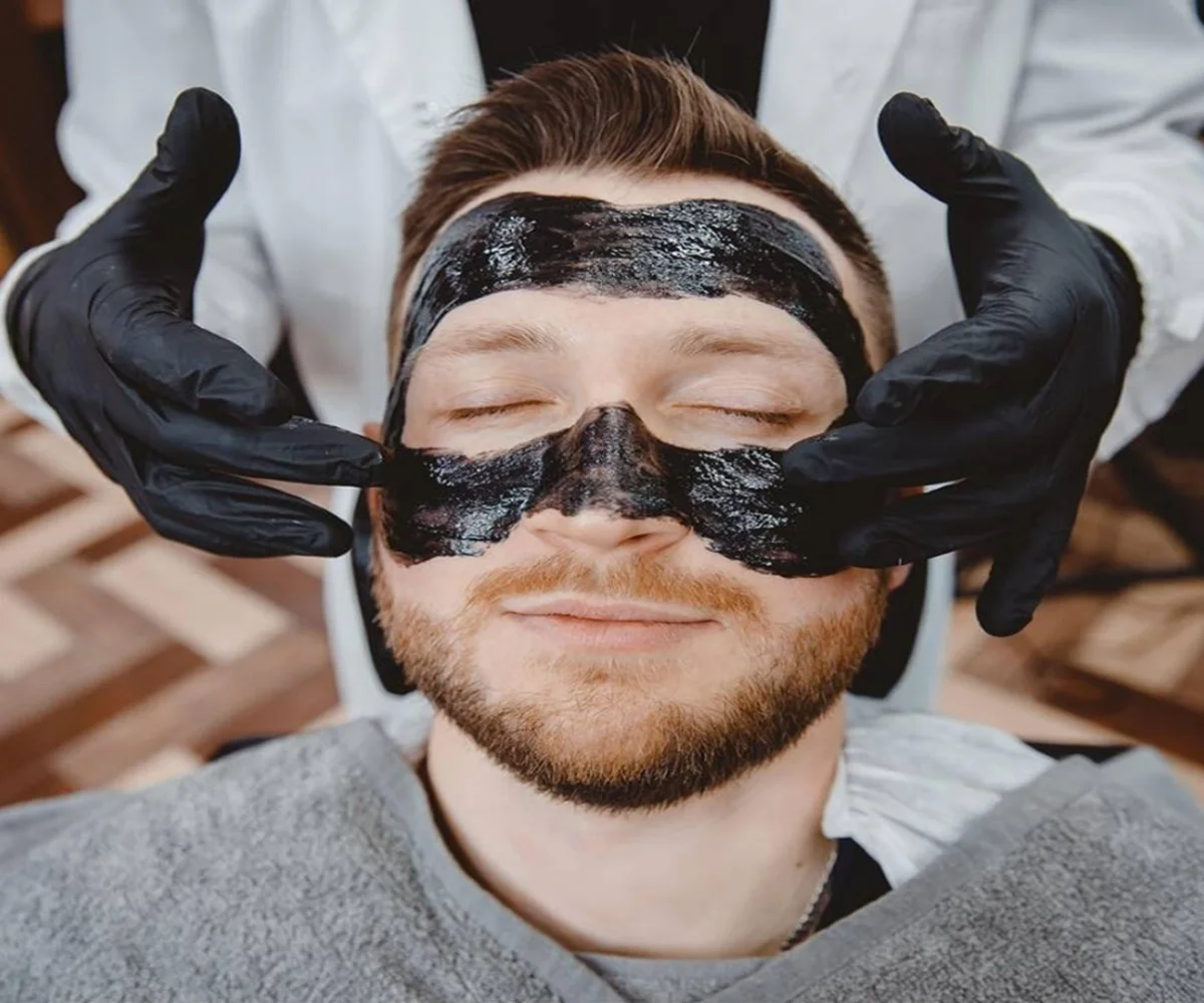 man in a salon with Black Mask for face treatment